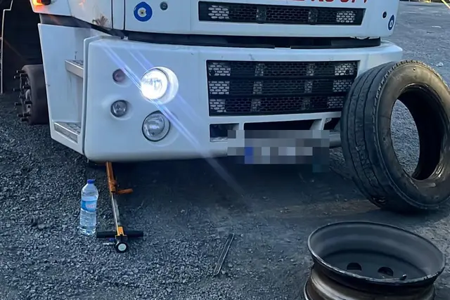 Bir kamyonun önü krikoyla kaldırılmış; sökülen lastik ve çıplak jant yanına konmuş, el aletleri yerde duruyor.